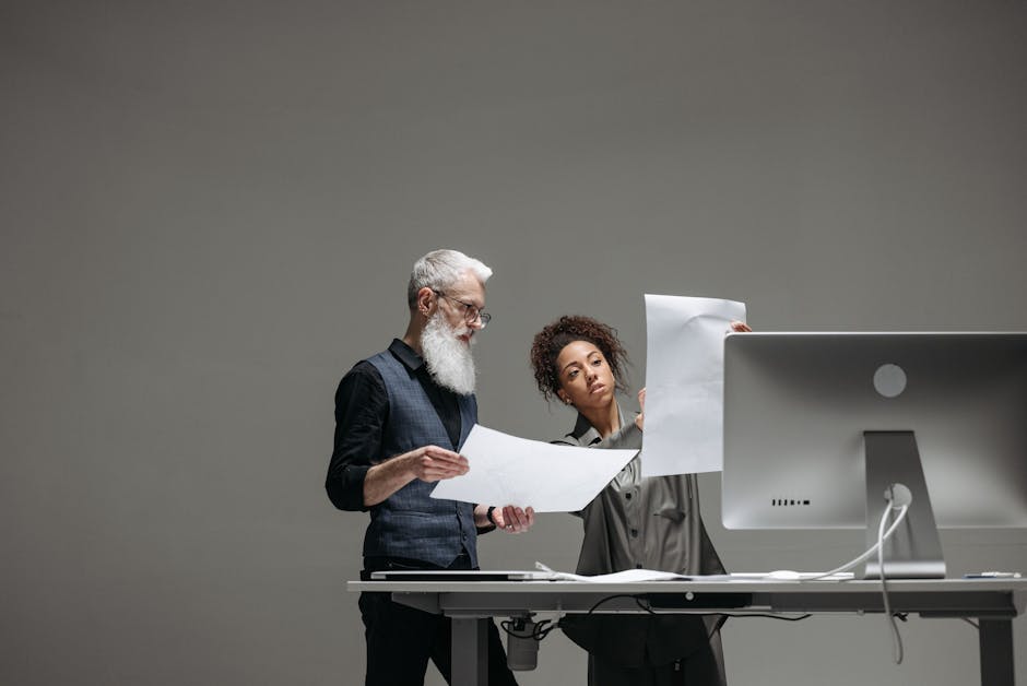 Two professionals collaborate on project plans at a computer workstation.