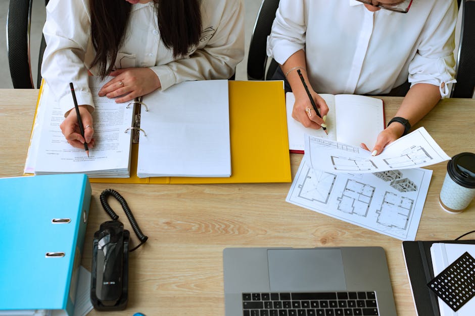 Two colleagues collaborating on architectural designs, reviewing plans and documents at a desk.